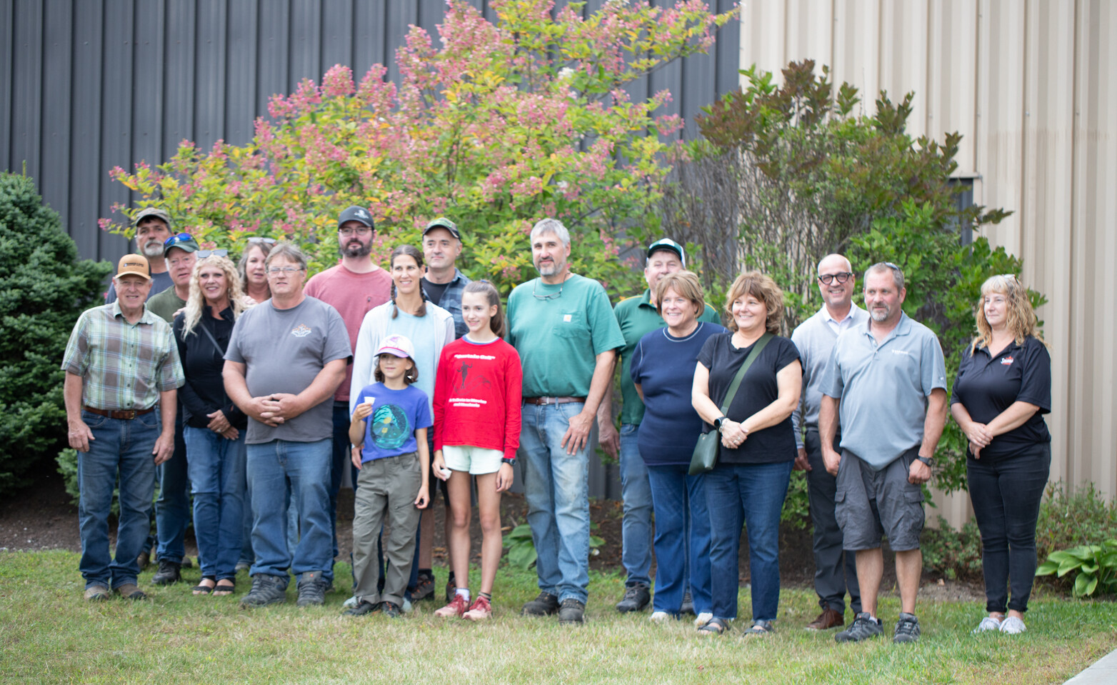 Group photo of 20 people outdoors, with a colorful bush in the background.