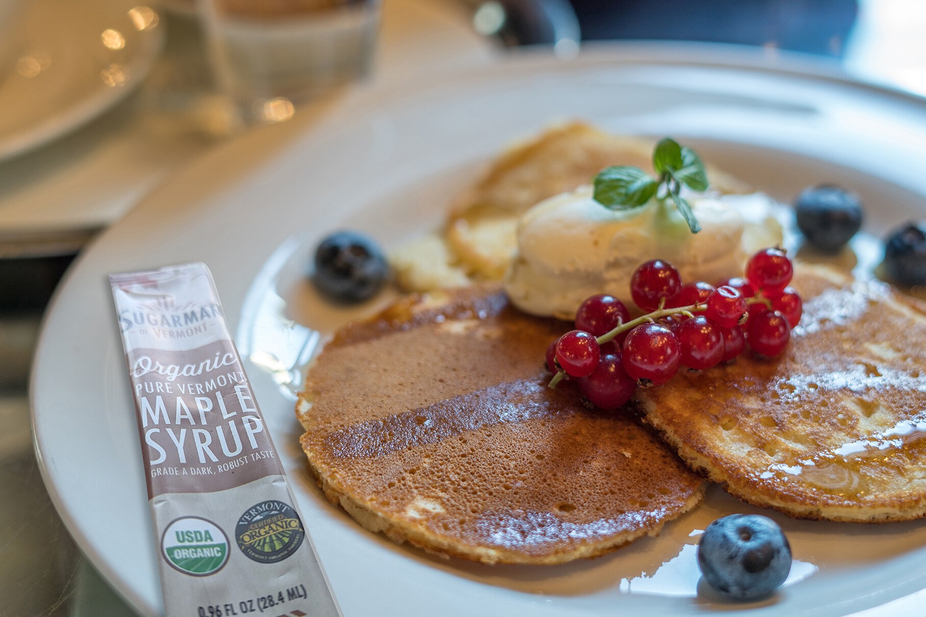 Pancakes topped with ice cream, berries, and a packet of maple syrup on a white plate.