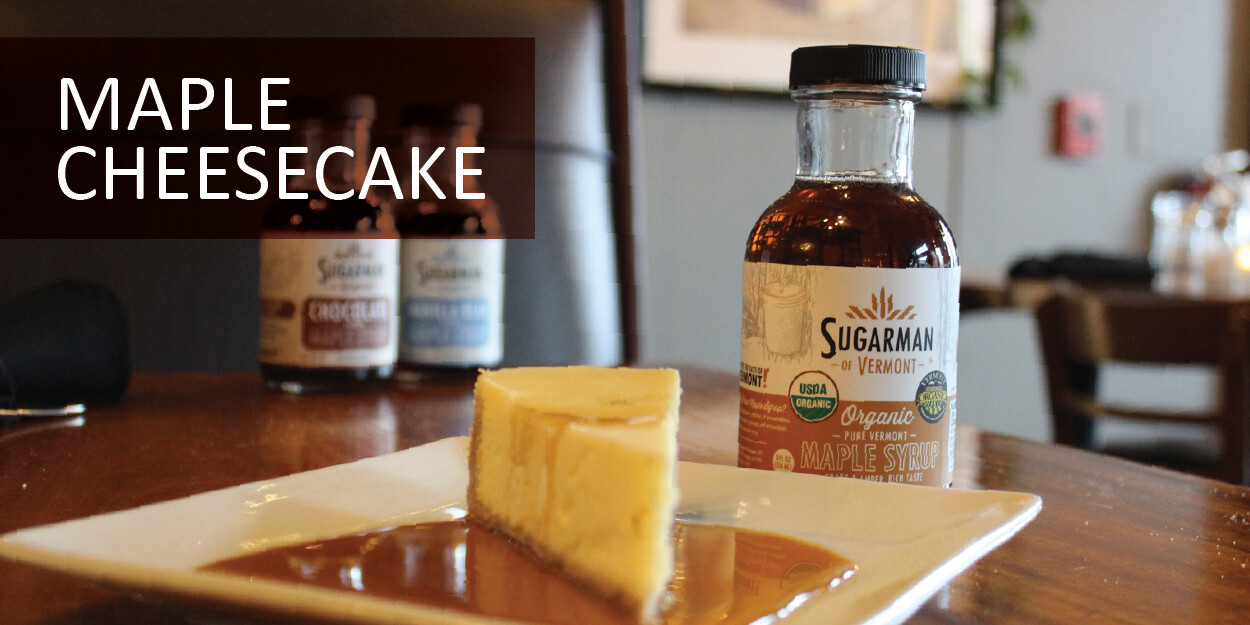 Bottle of maple syrup beside a slice of maple cheesecake on a plate.