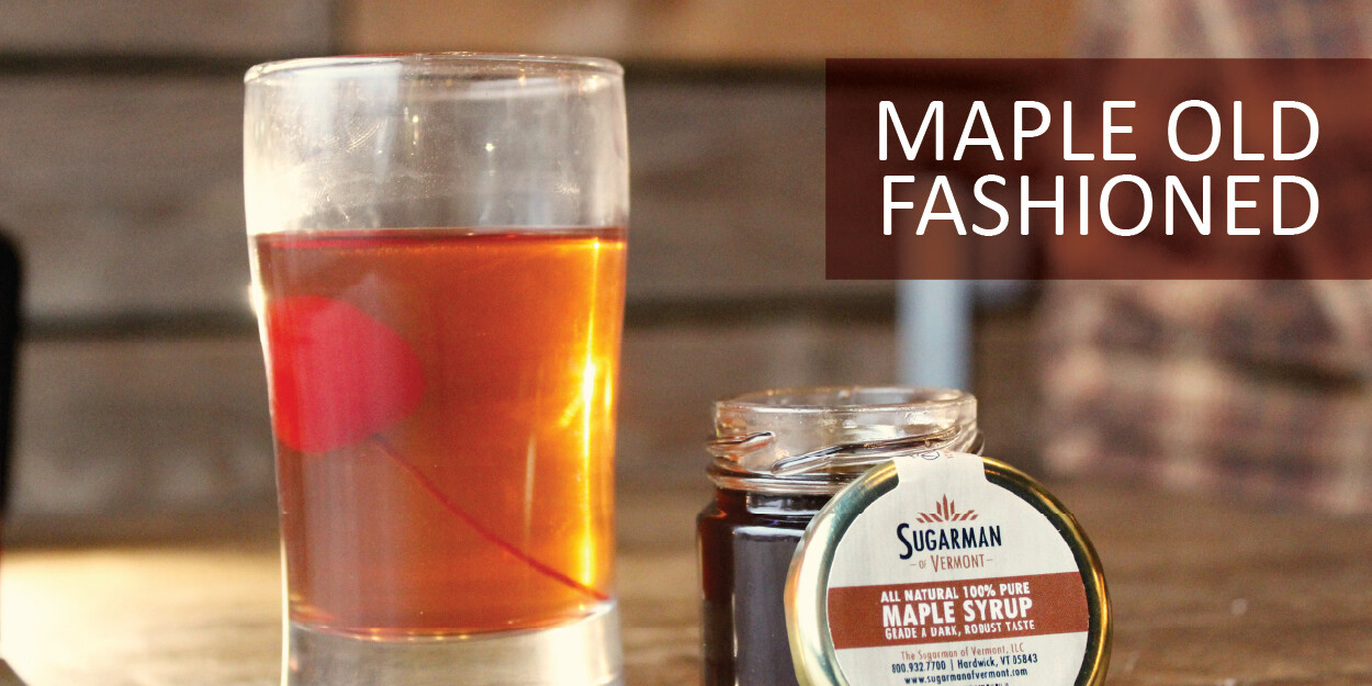Glass of Maple Old Fashioned with a cherry and jar of maple syrup on a table.