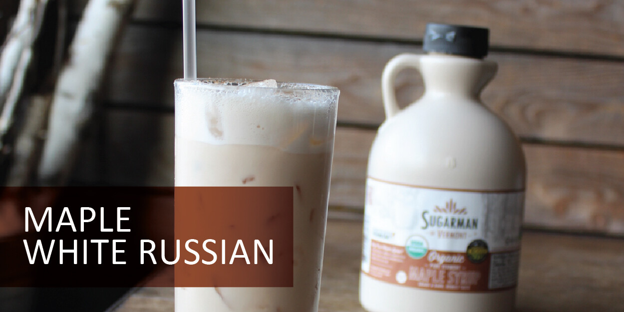 A glass of iced Maple White Russian and a bottle of maple syrup on a wooden background.