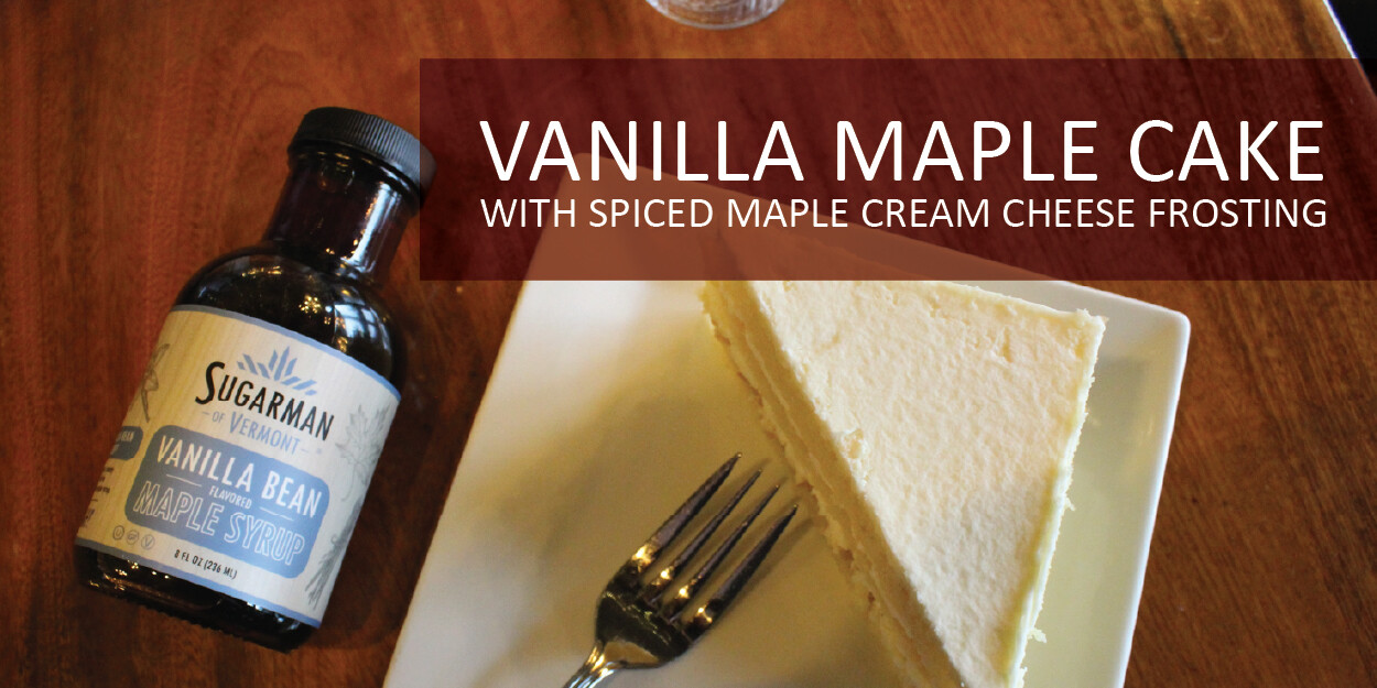 Slice of vanilla maple cake with spiced maple cream cheese frosting and maple syrup bottle.