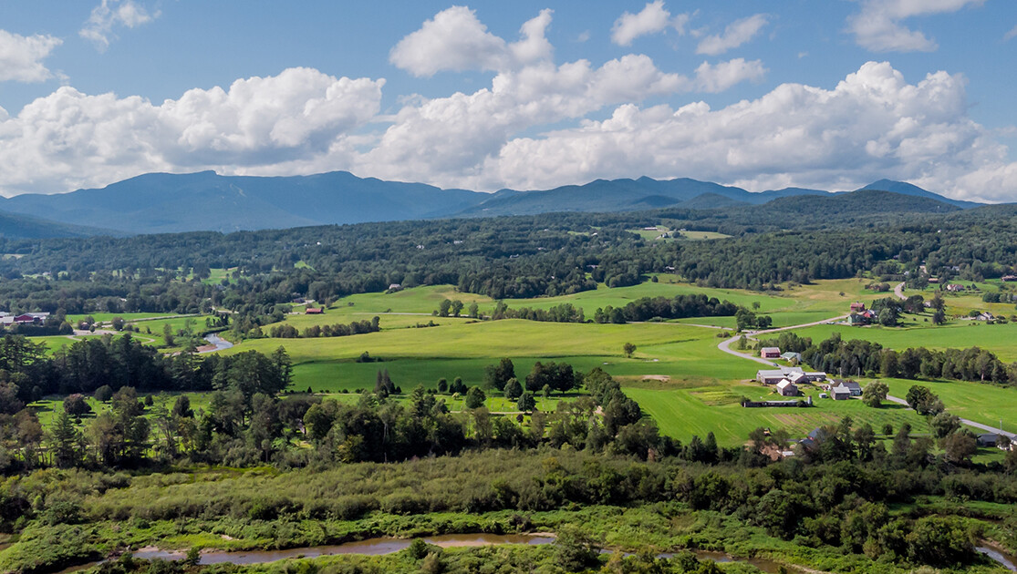 A scenic landscape of green fields and hills under a cloudy sky.
