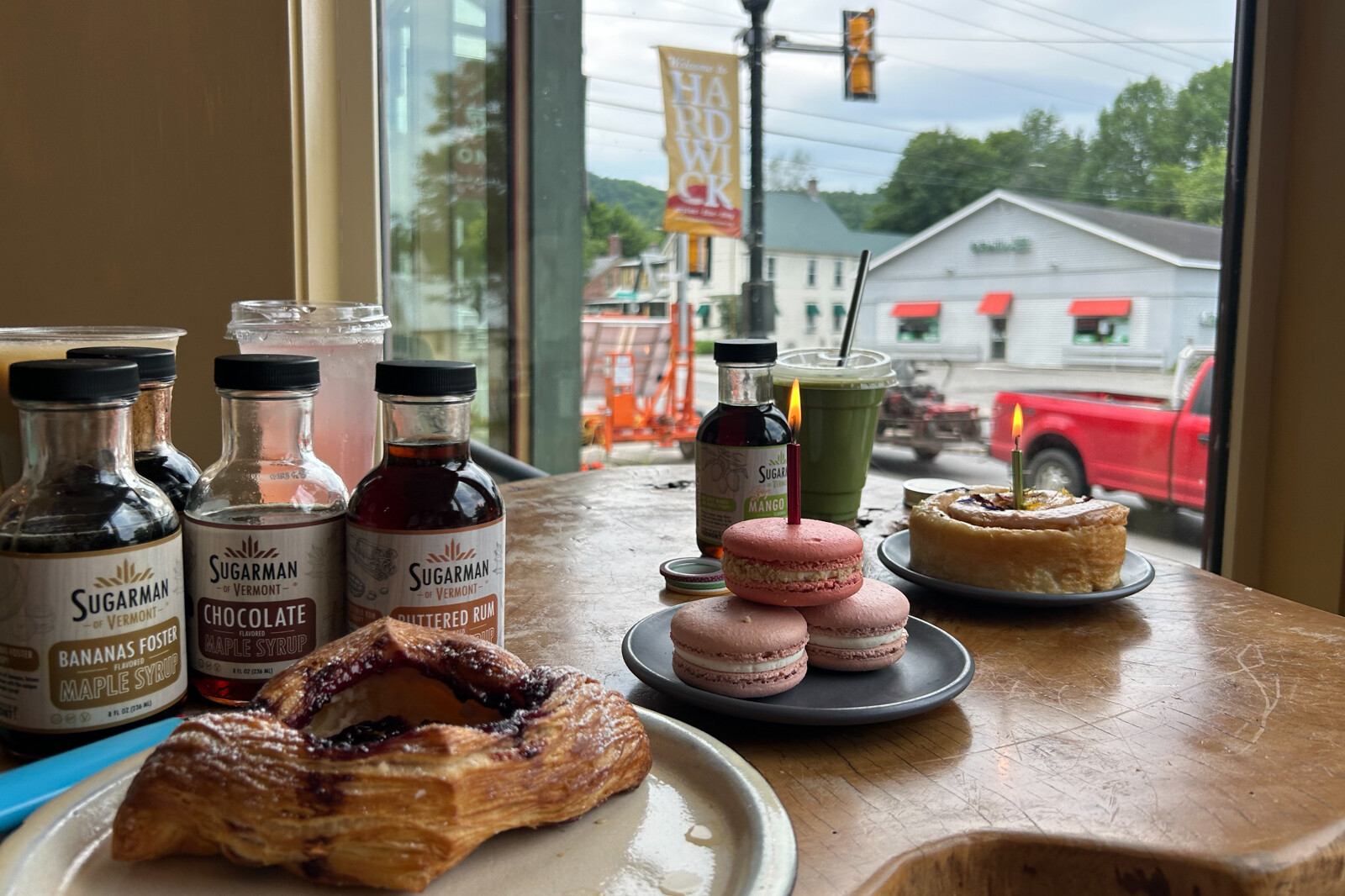 Pastries and flavored syrups on a wooden table with a view of a street outside.